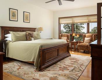 King bed with a light green bedspread with a medium wood Head and footboard. Large windows with a view of the Mountains 